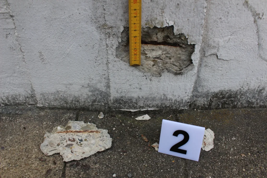 Betonabplatzung an Wand mit Messung und Schadensmarkierung – Begutachtung von Bauschäden durch Sachverständigen