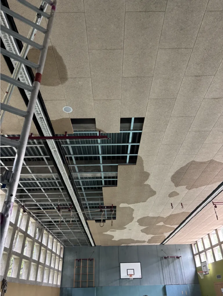 Großflächiger Wasserschaden an Hallendecke mit durchnässten Deckenplatten und Öffnungen